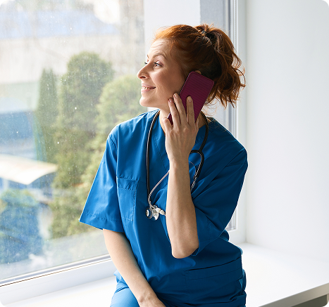 Nurse in blue scrubs smiling while speaking on the phone by a window, representing Amity’s supportive communication and care.