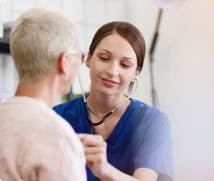 Nurse in blue scrubs listening to a patient’s heartbeat with a stethoscope, providing compassionate care.