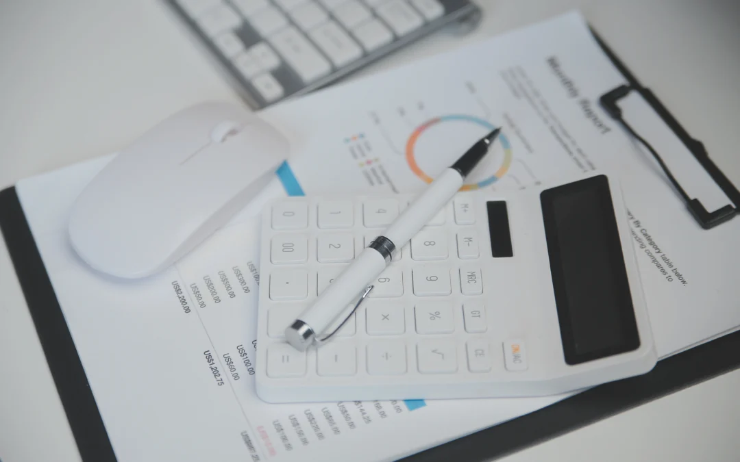 Close-up of a white calculator and pen resting on financial documents with a colorful chart in the background on a desk.